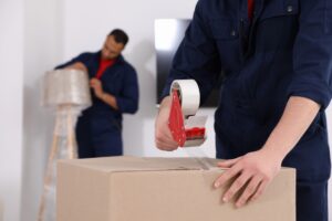 Male mover packing box with adhesive tape in house, closeup. Space for text